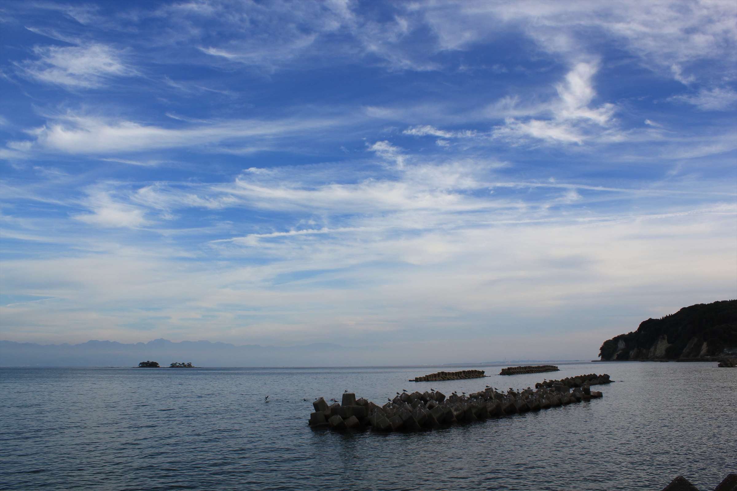 青空と白い雲、テトラポッドが並ぶ富山湾の風景