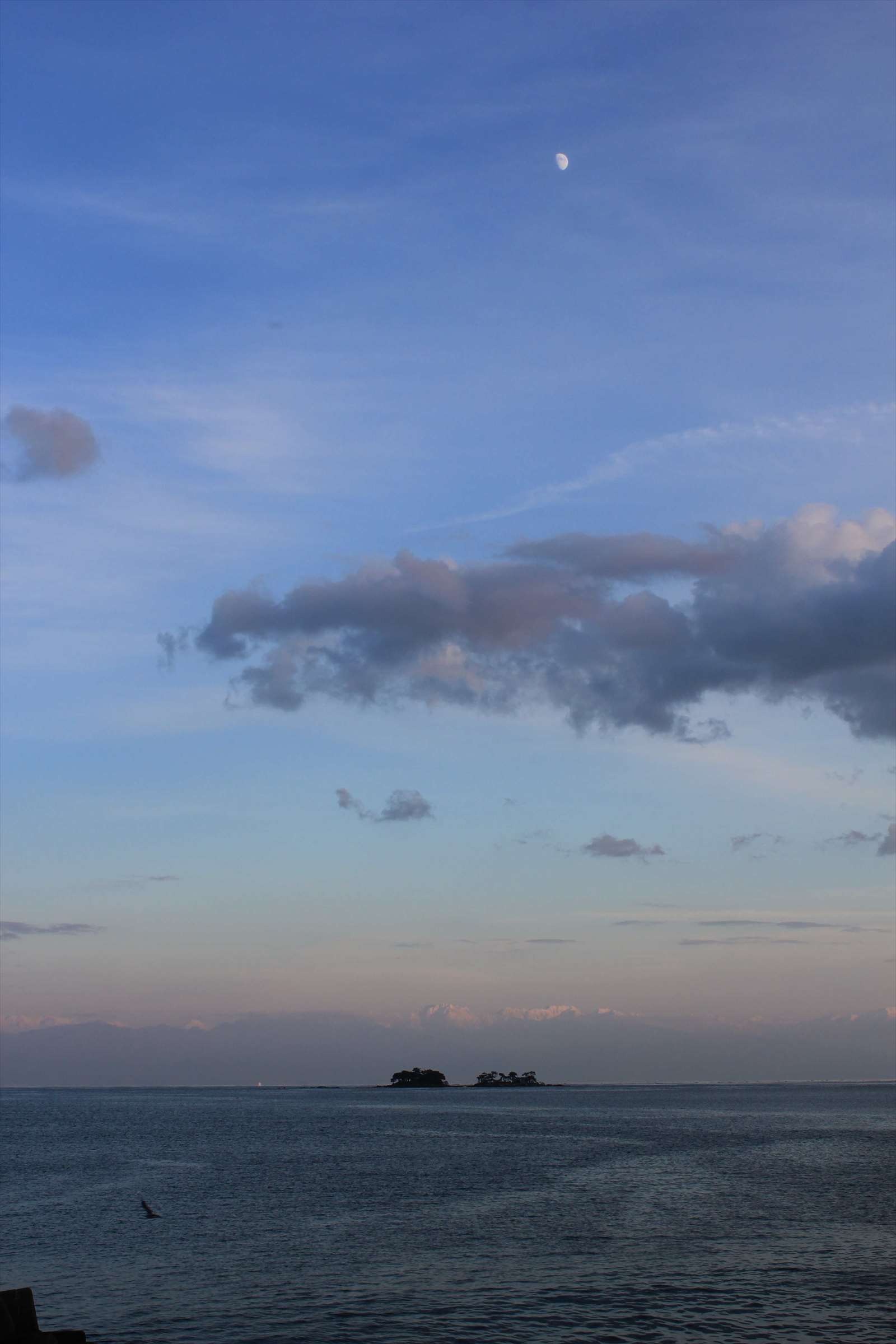 夕暮れ時の海に浮かぶ月と小島のシルエット
