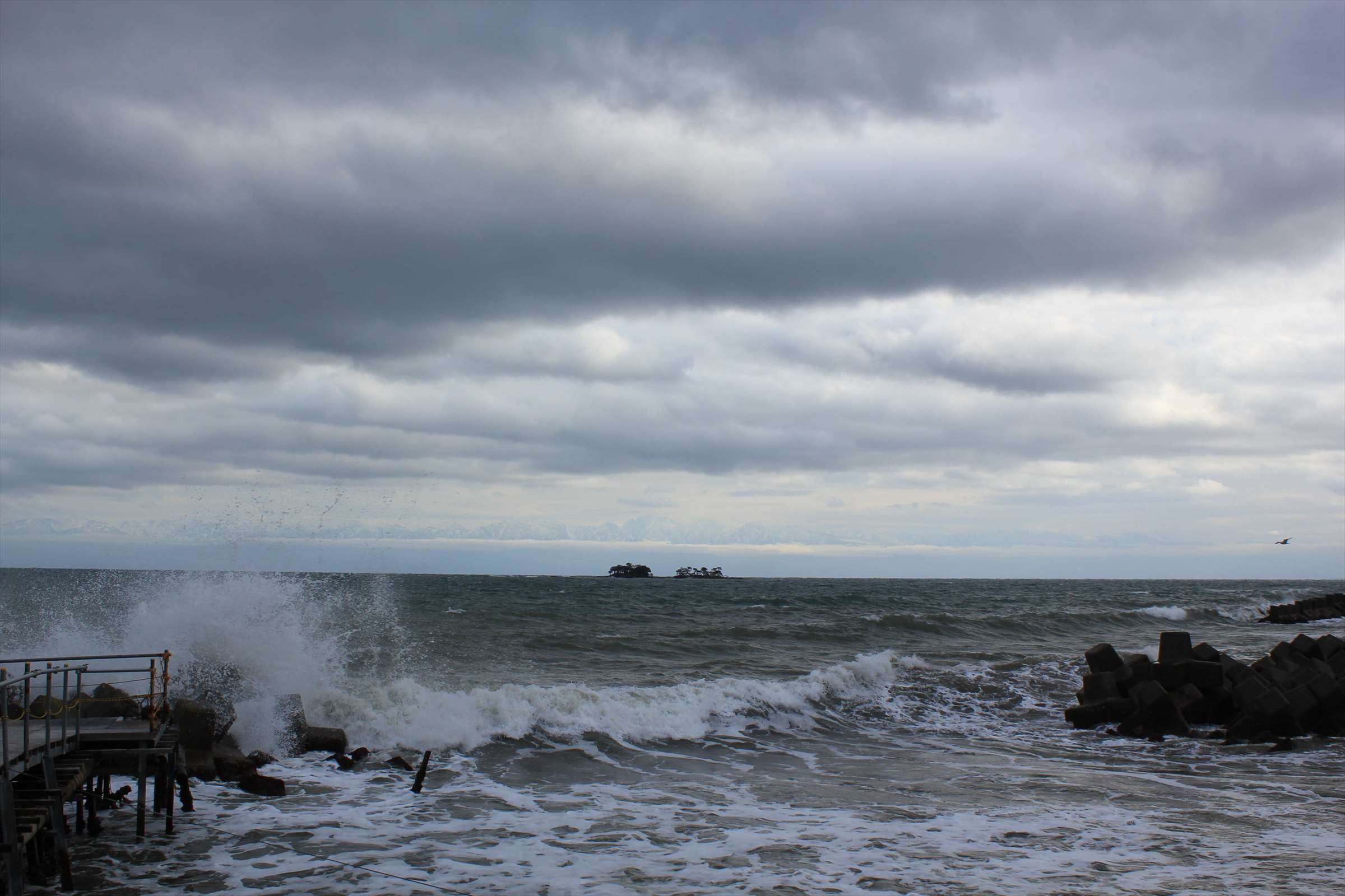 荒波と曇り空、テトラポッドと桟橋がある冬の海岸
