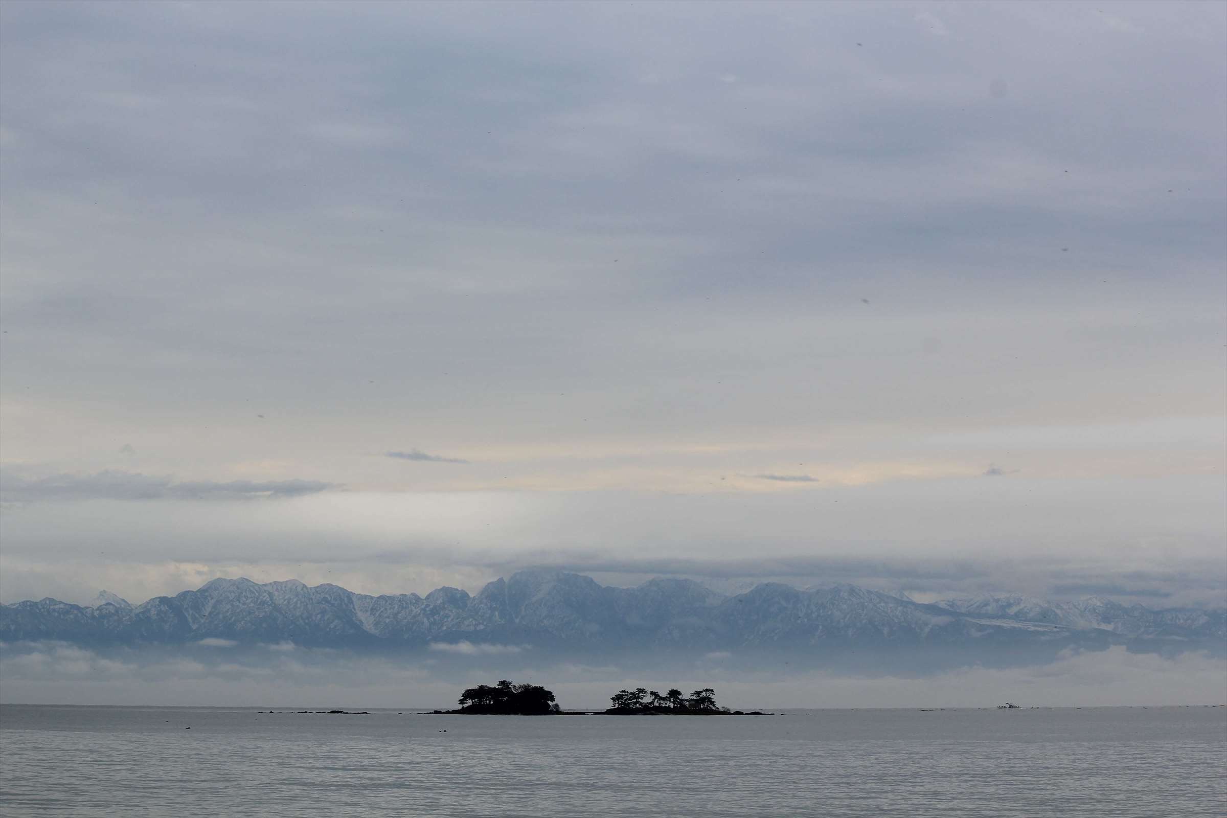 曇り空と立山連峰、海に浮かぶ小島のシルエット