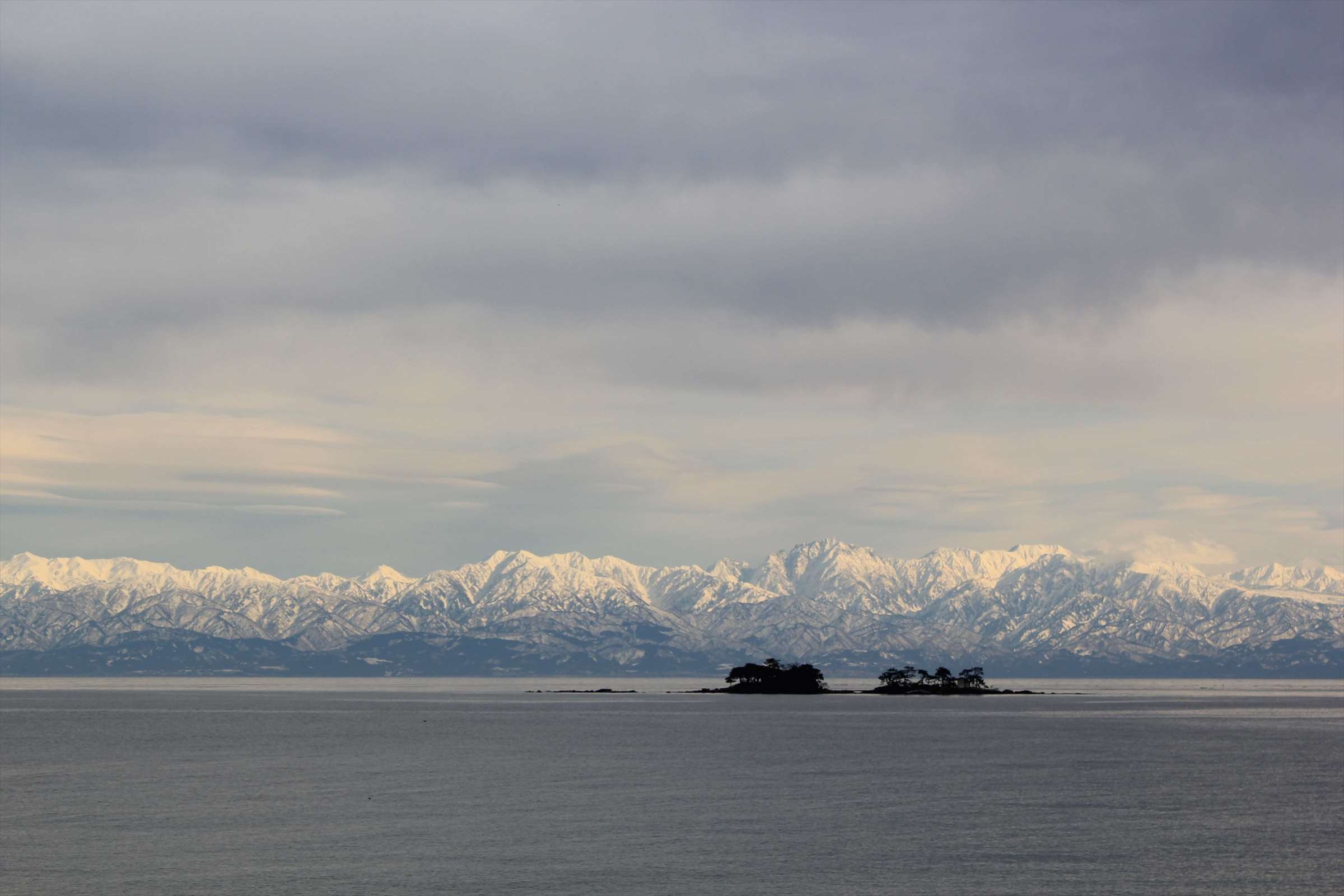 雪をいただいた立山連峰と小島、冬の富山湾