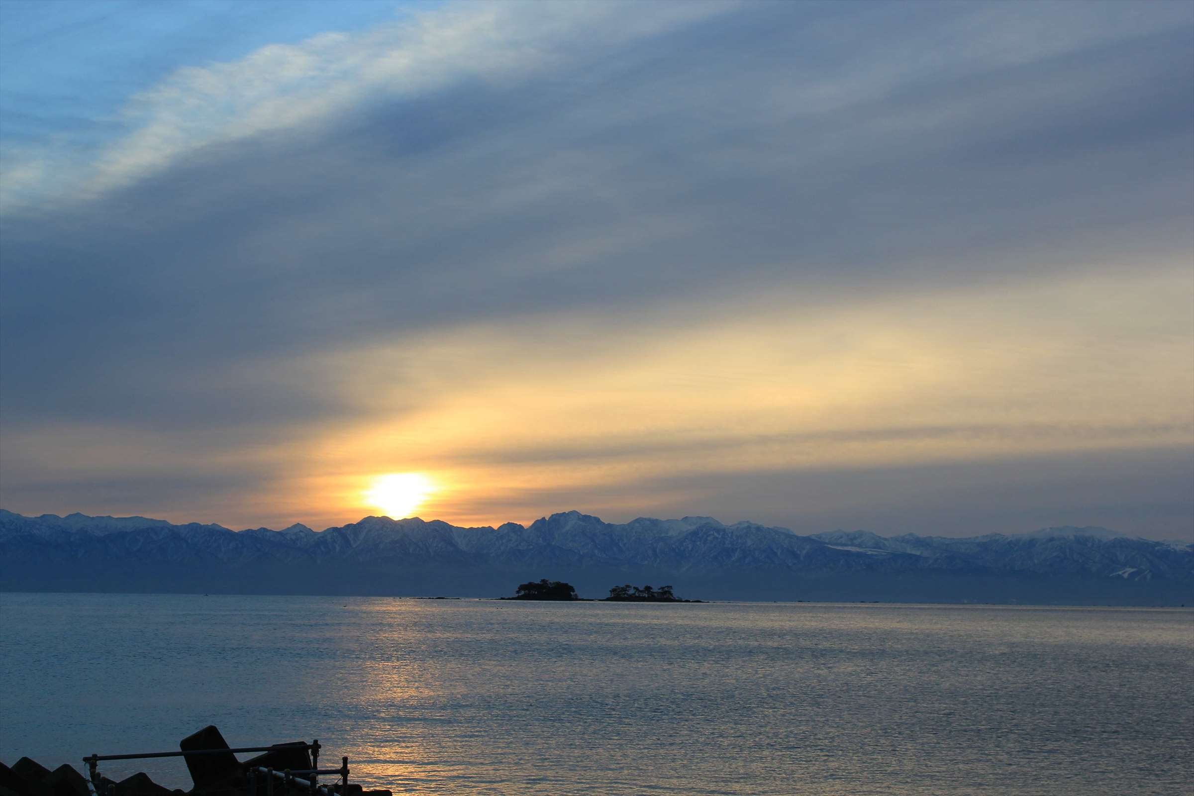 夕暮れ時の立山連峰と小島、沈む夕日の富山湾