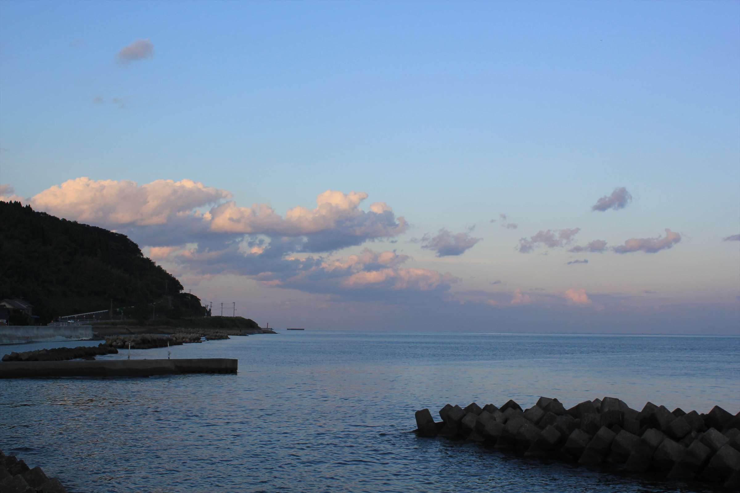 夕暮れ時の港と防波堤、岬が見える富山湾