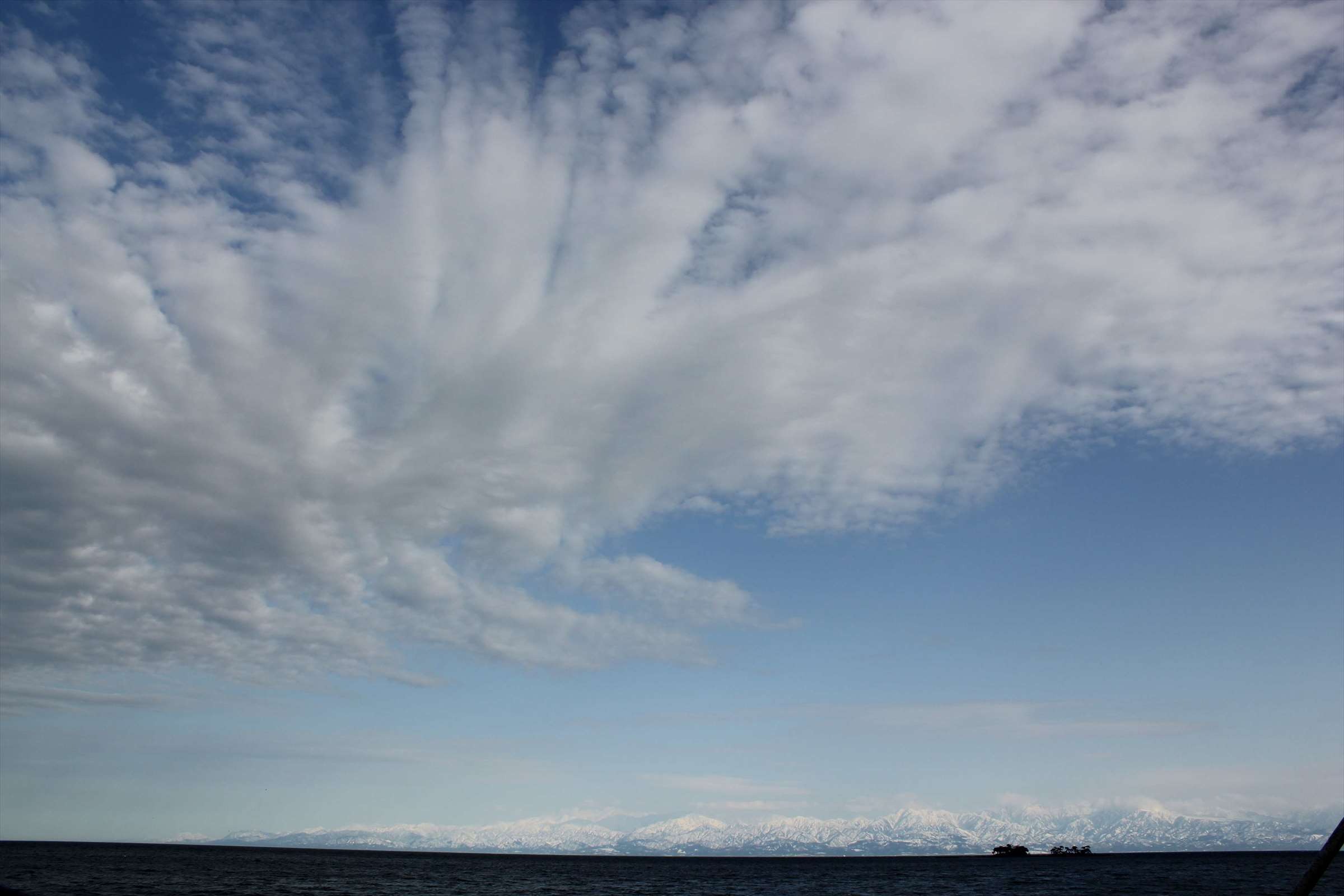 青空と立山連峰に広がる羽状の雲と富山湾
