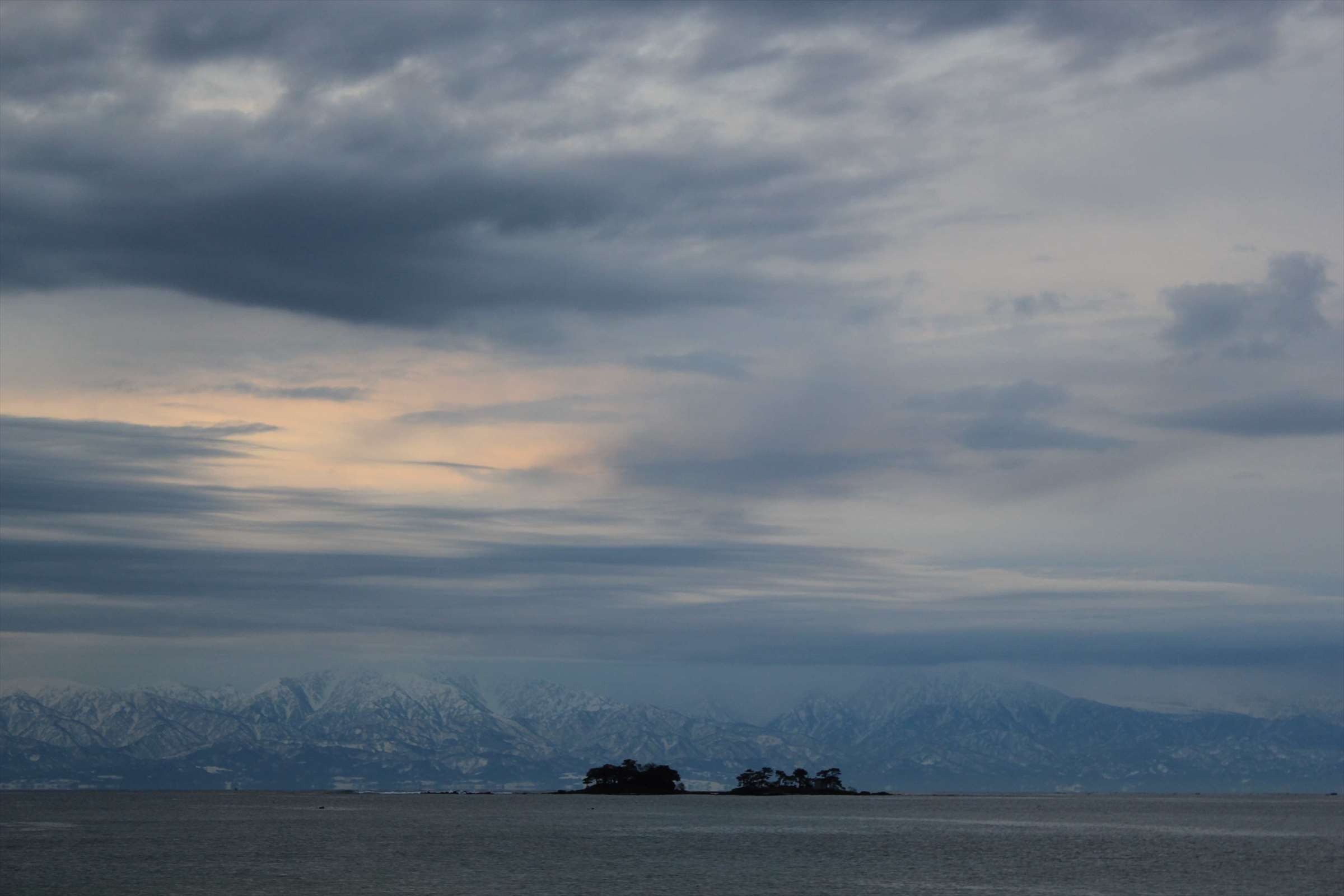 曇り空と立山連峰のシルエット、穏やかな富山湾と小島