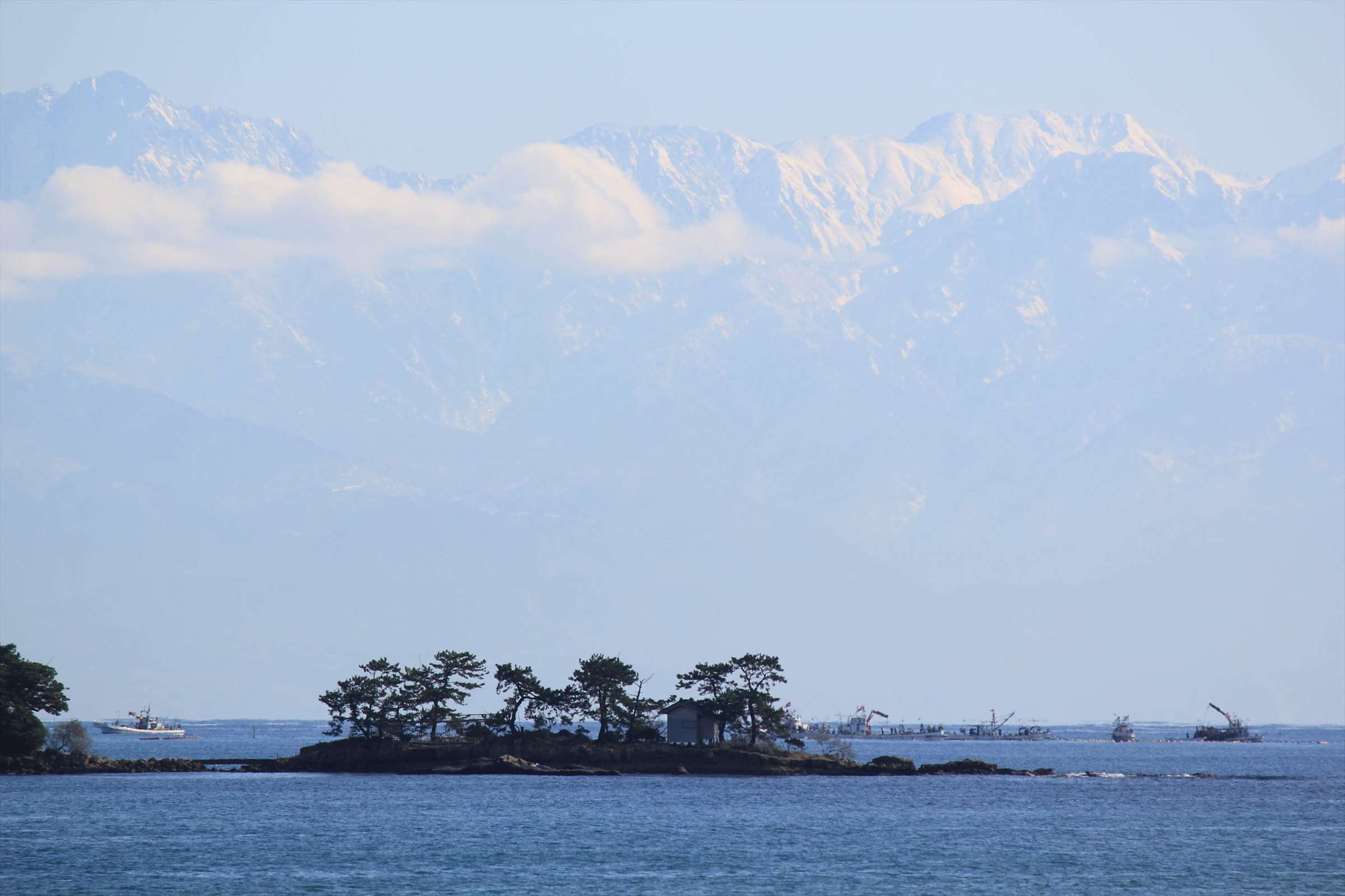 立山連峰と小島、漁船が行き交う富山湾