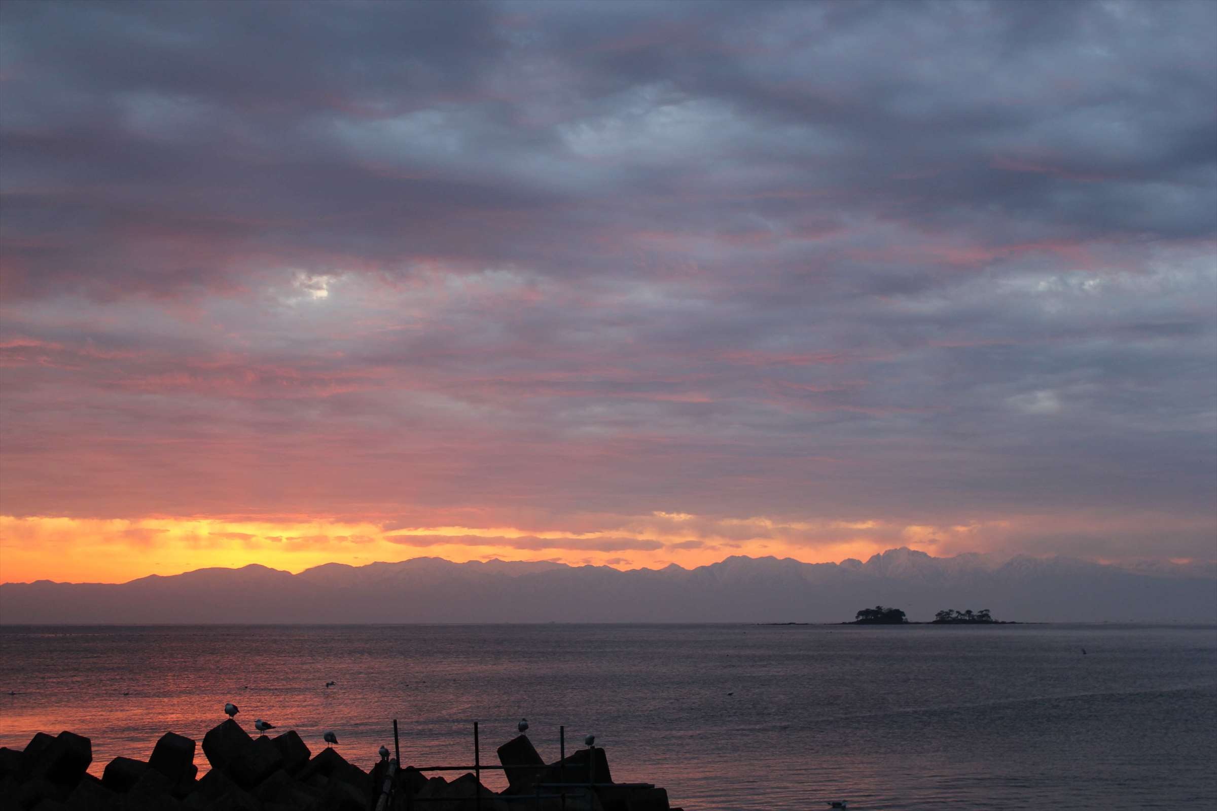 夕焼けに染まる空と富山湾、小島のシルエット