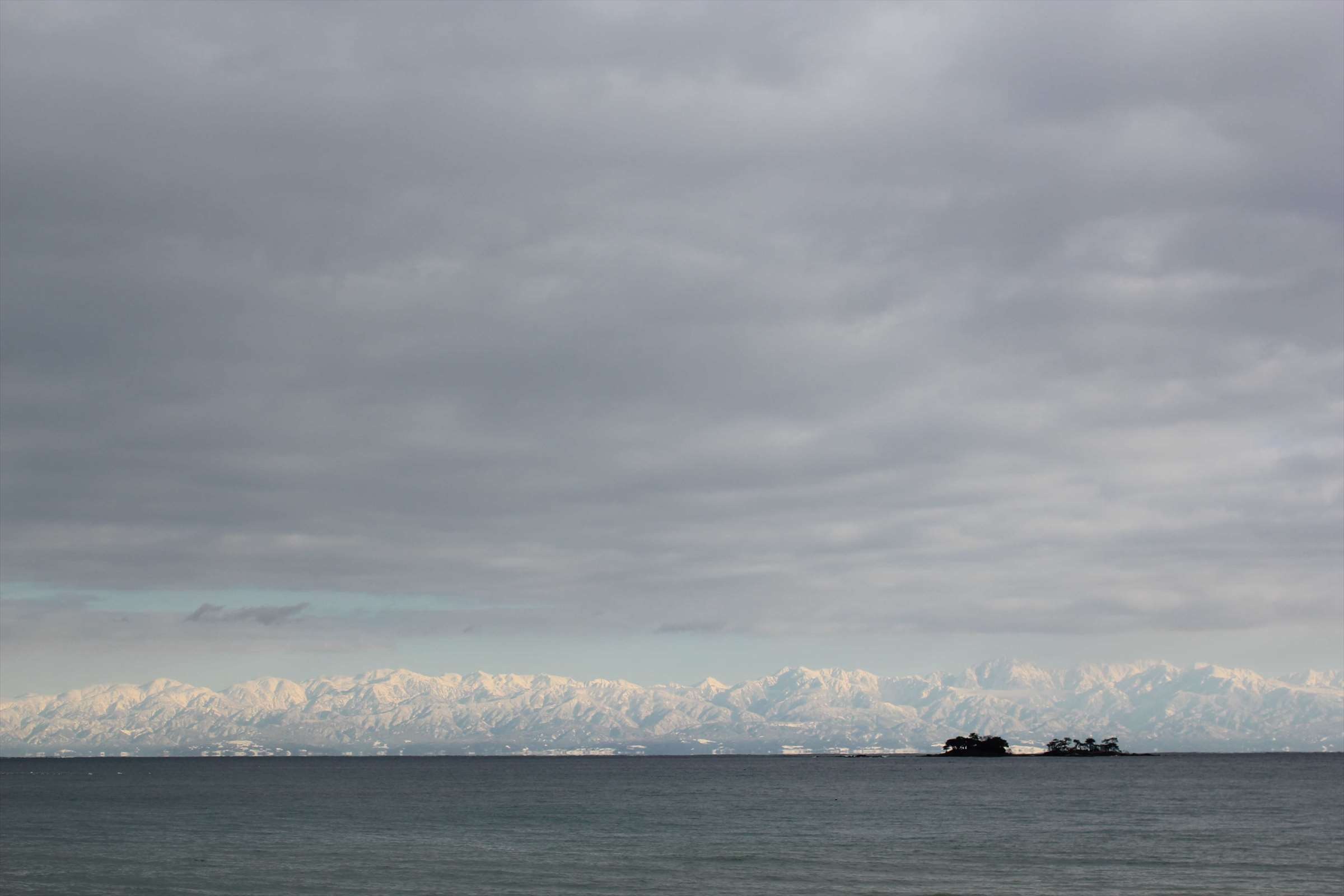 曇り空に望む立山連峰と小島、穏やかな富山湾