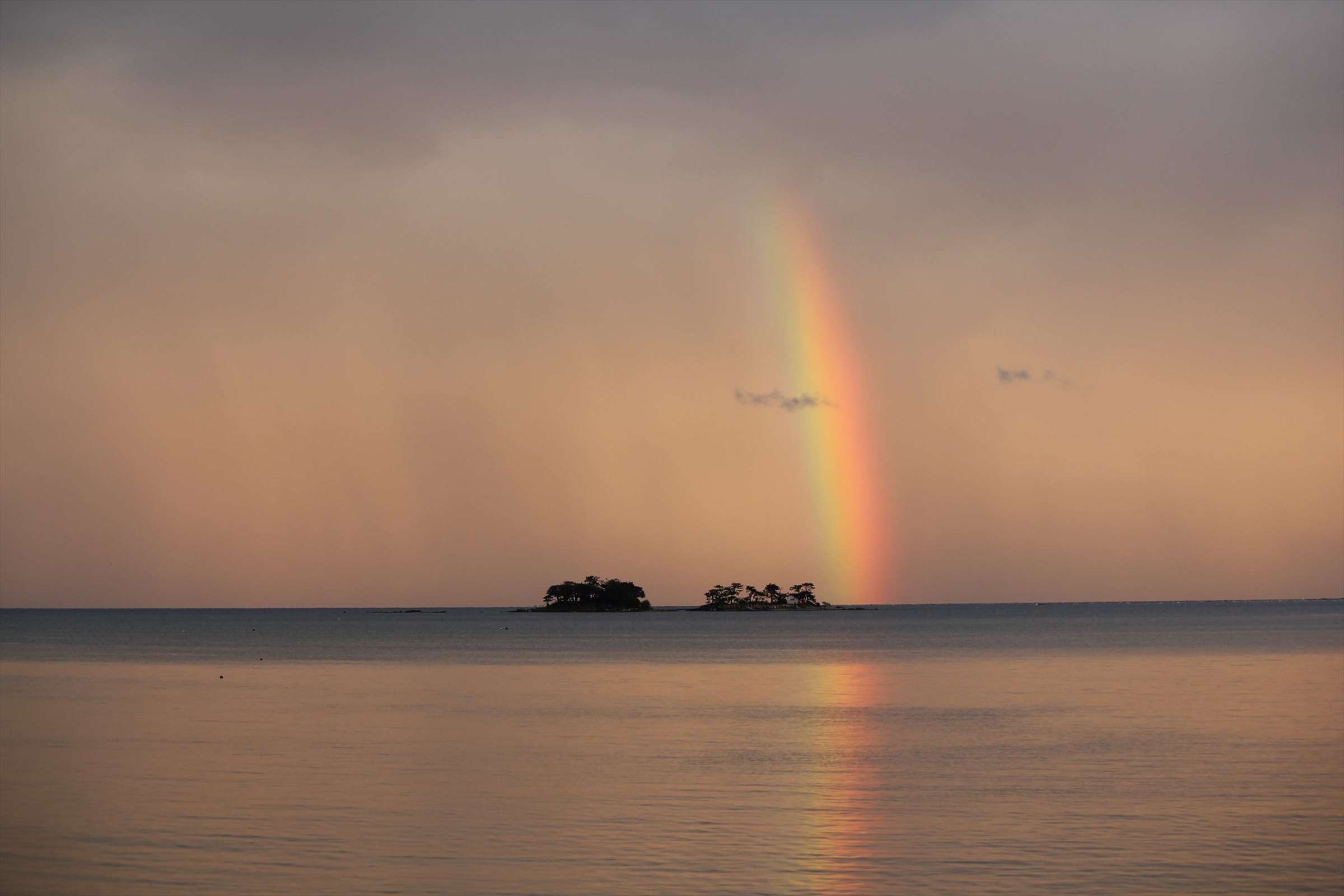 小島に架かる虹と夕焼けの富山湾