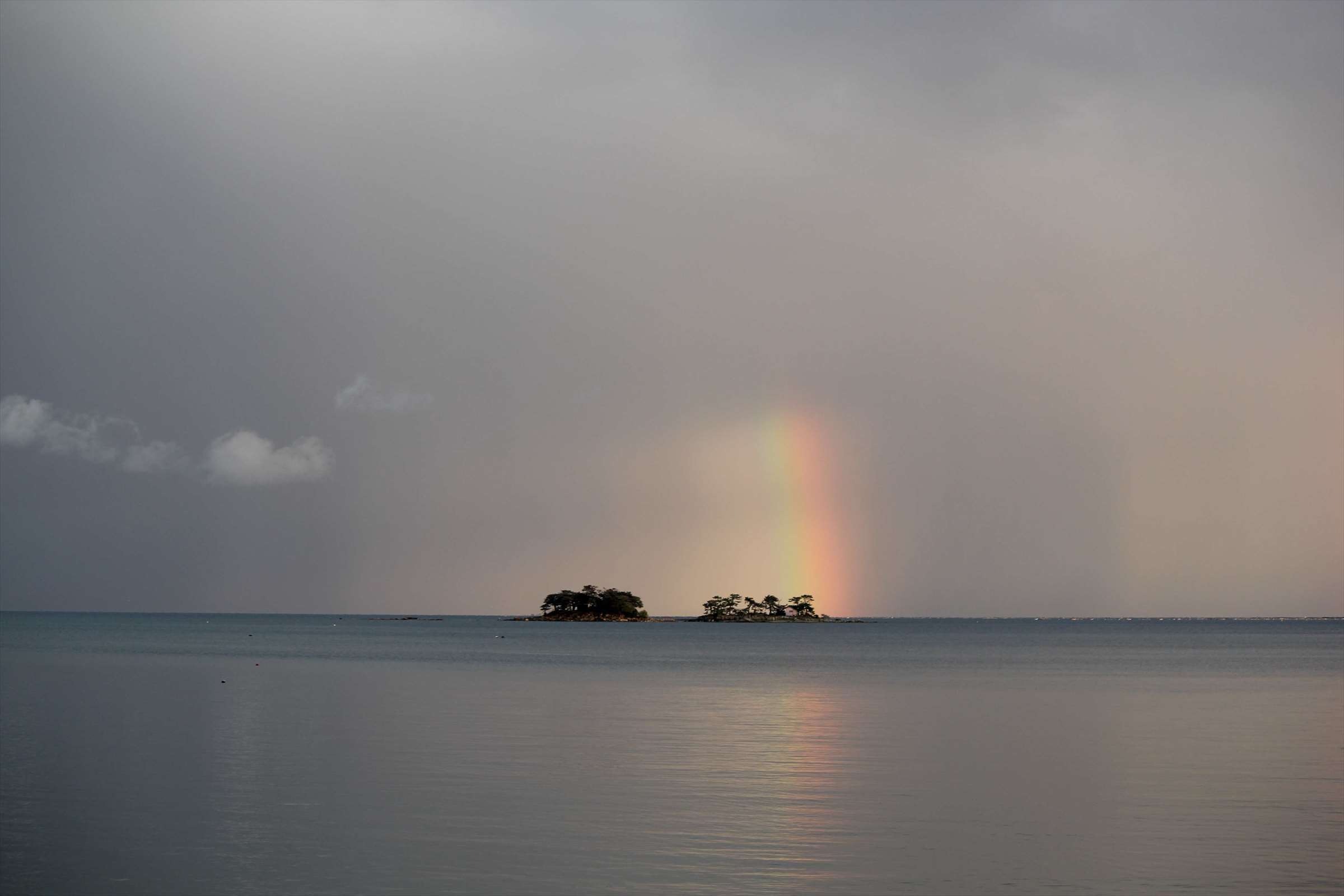 小島に架かる鮮やかな虹と曇り空の富山湾