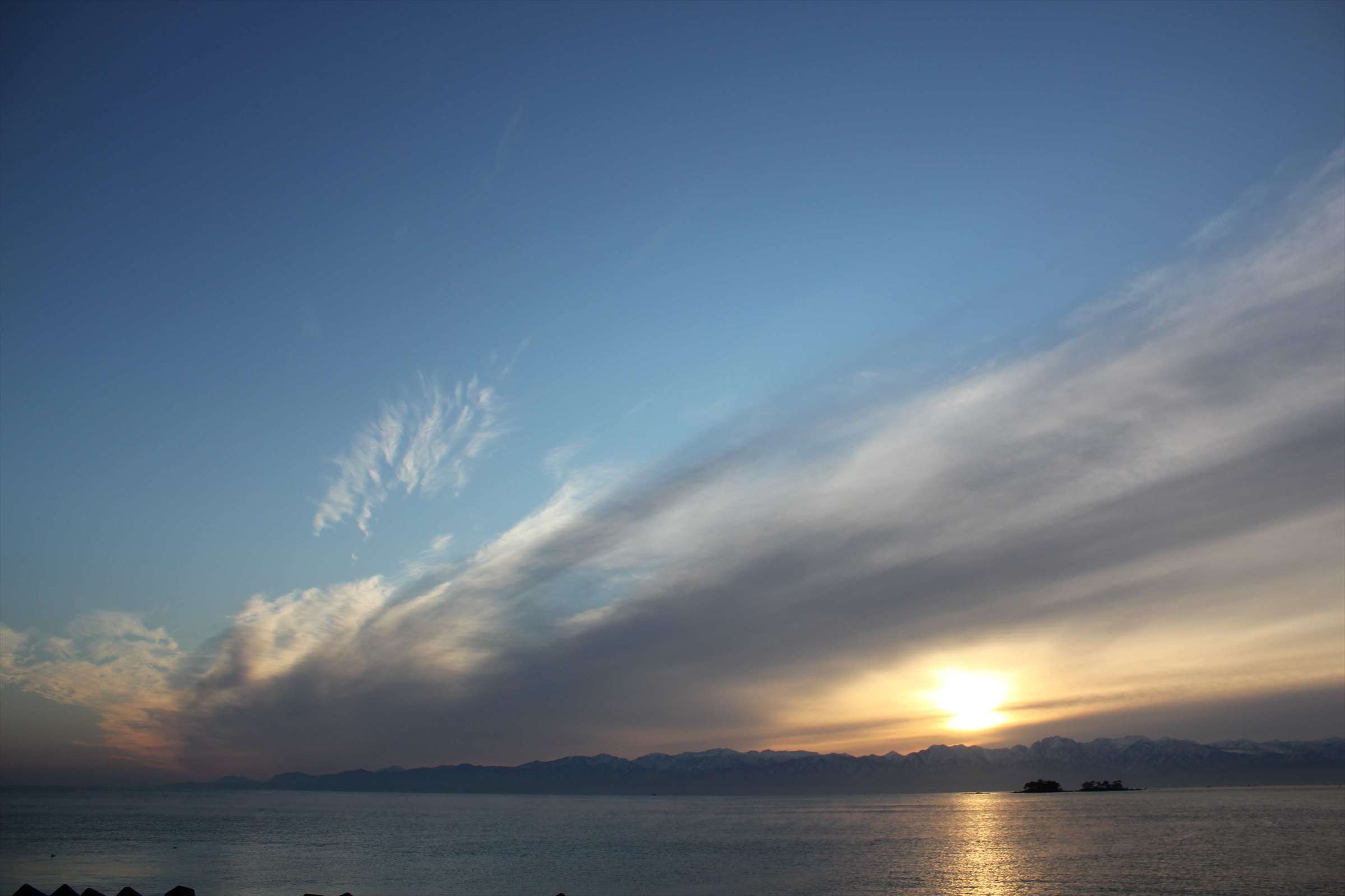 夕日が沈む富山湾、立山連峰と流れる雲