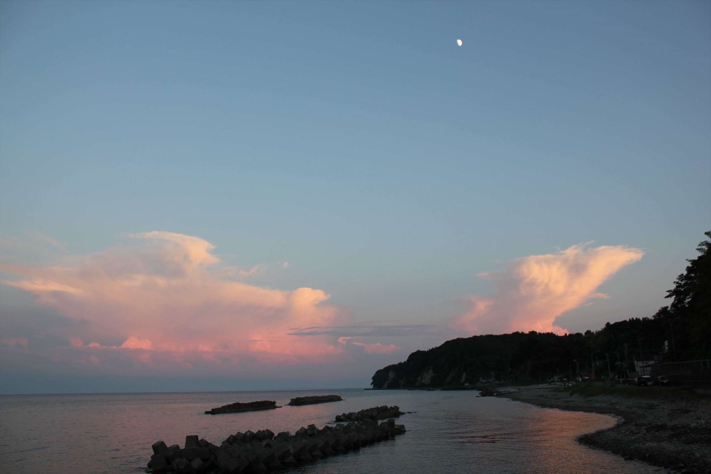 夕暮れに月と入道雲がピンクに染まる富山湾の海岸