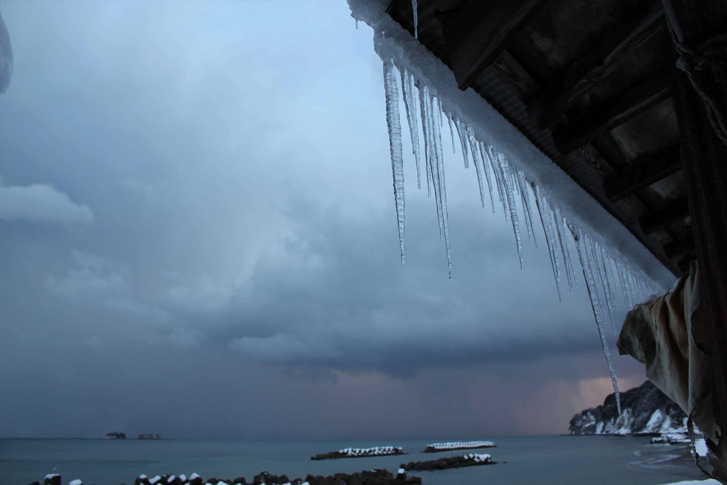 屋根のつらら越しに見る冬の富山湾と荒れた海