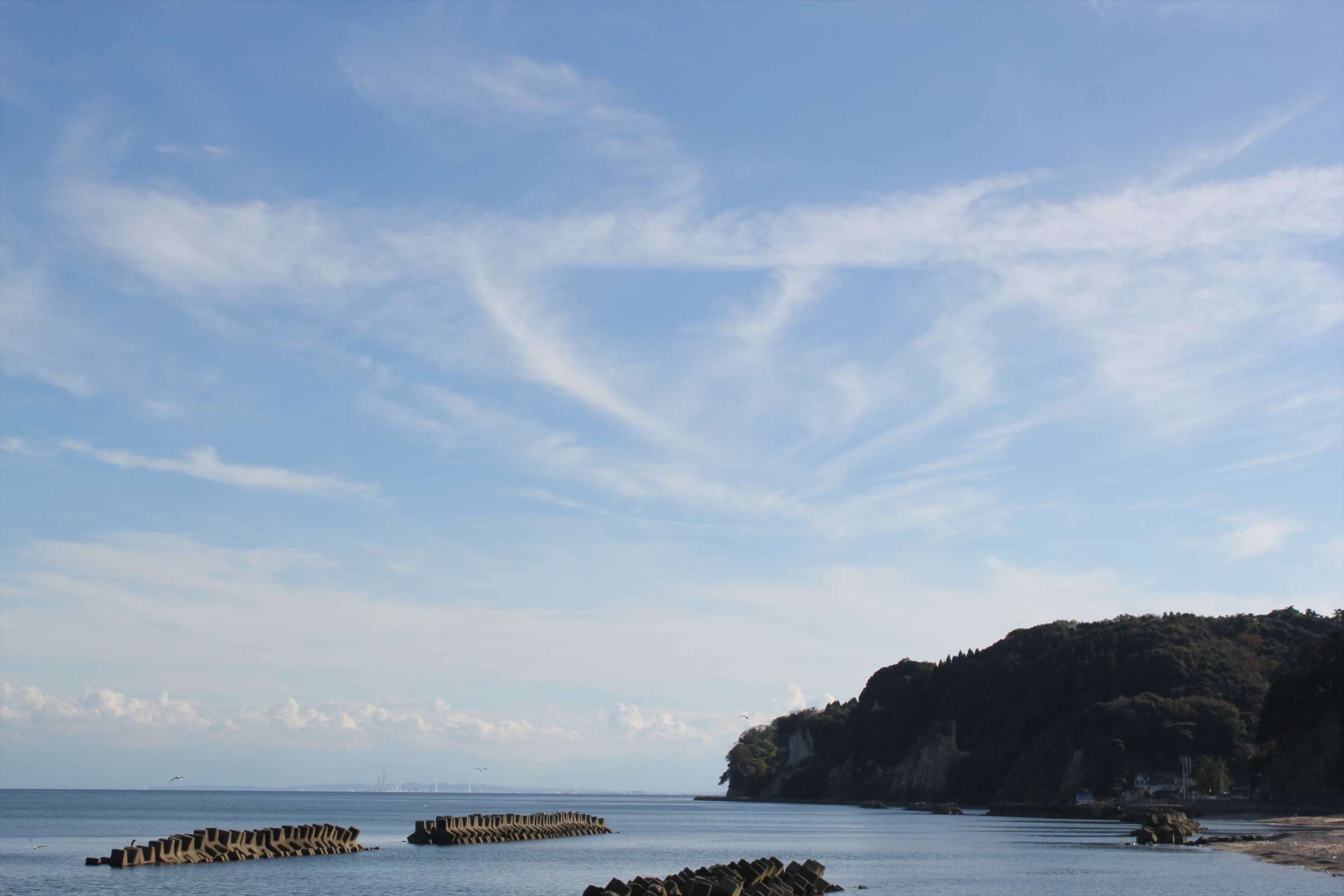 青空に飛行機雲が描かれた富山湾の海岸
