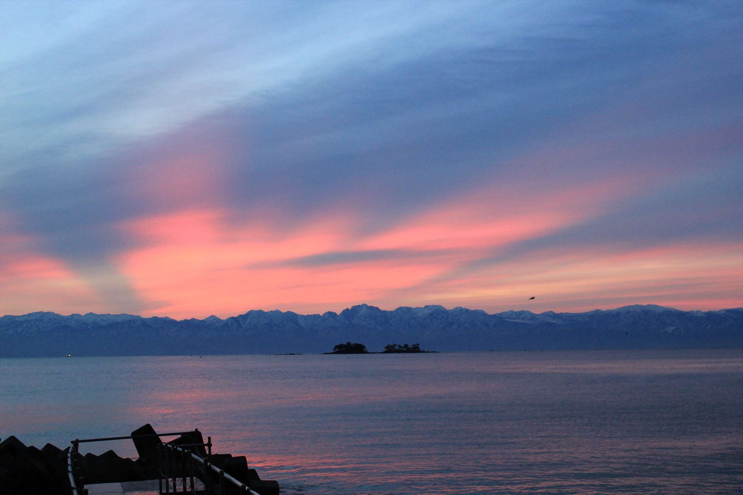夕焼けに染まる空と立山連峰、小島のシルエット