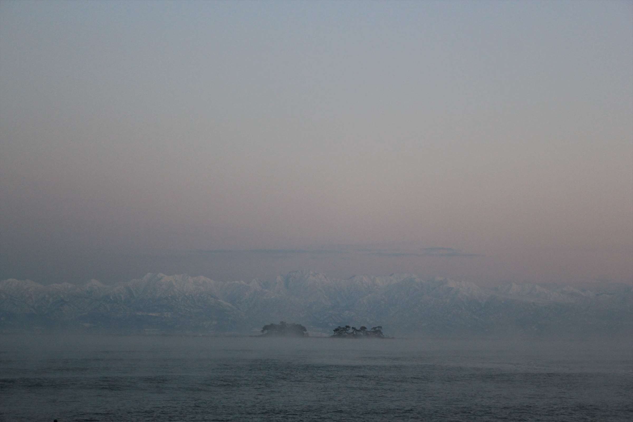 朝霧に包まれた立山連峰と小島、富山湾の夜明け