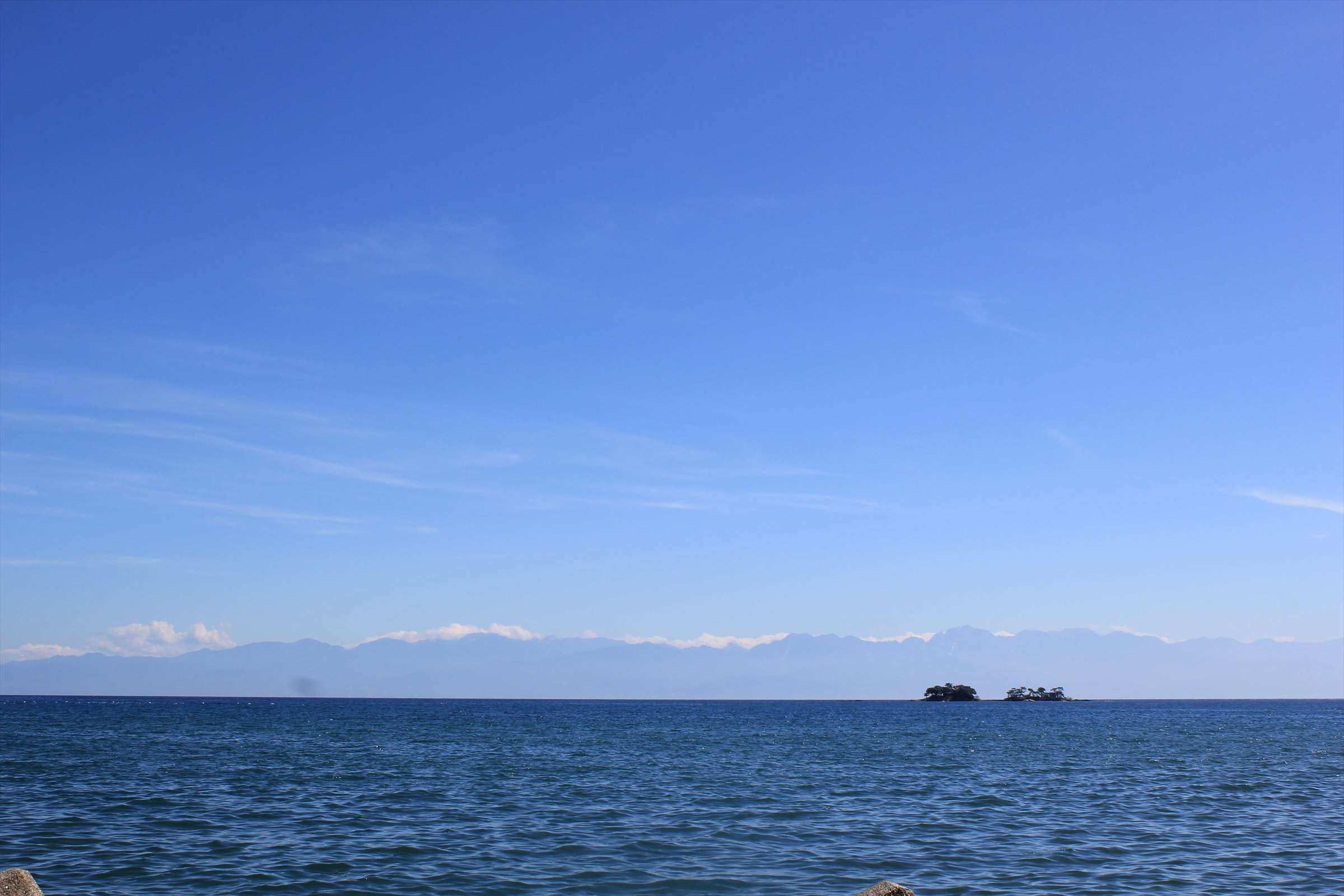 青空と穏やかな富山湾、立山連峰と小島の遠景
